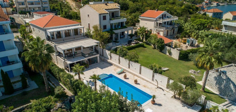 Villa in Krašići, Montenegro: top view of the house with a pool, terrace, green garden, and palm trees by the sea.