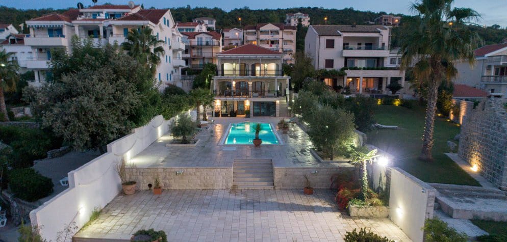 Villa with a pool and terrace in Krašići, Montenegro: view of the illuminated house facade and landscaped grounds in the evening.