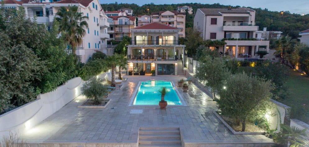 Three-story villa with a pool and terrace in Krašići, Montenegro: view of the house with lighting, a garden, and a lounge area.