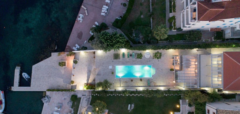 Aerial view of a villa with a pool and private beach in Krašići, Montenegro: night lighting and a seaside terrace.