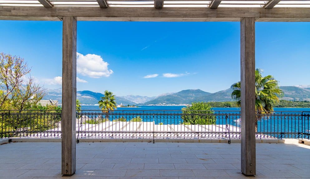 Villa terrace in Krašići, Montenegro: panoramic view of the sea, mountains, and island, with a wooden pergola and wrought-iron railing.