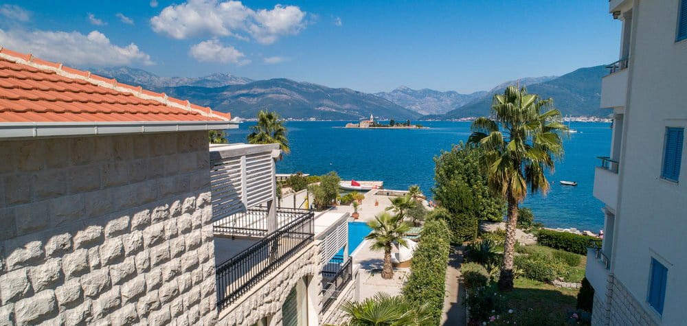 View from the villa terrace in Krašići, Montenegro: pool, palm trees, and panoramic sea and island views in the Bay of Kotor.