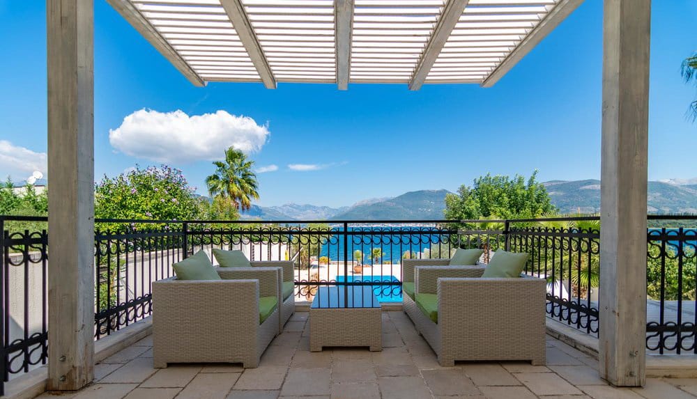 Villa terrace in Krašići, Montenegro: wicker furniture, awning, and panoramic sea and mountain views.