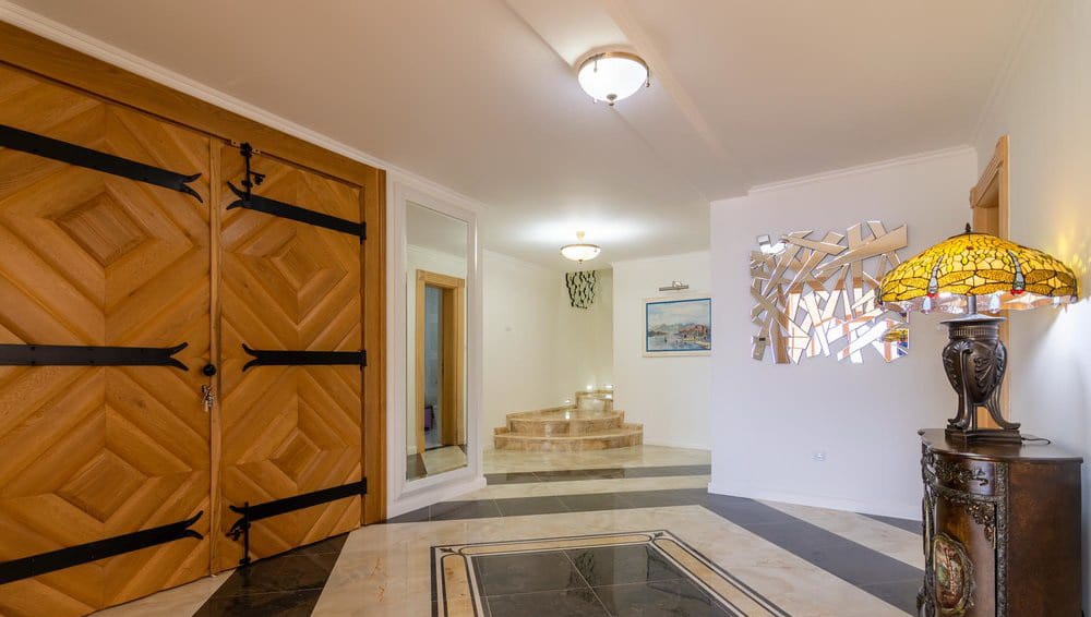 Spacious villa hallway in Krašići, Montenegro: marble floor, solid wooden doors, and a designer lamp.