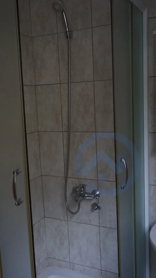 Shower enclosure with beige tiles, chrome mixer tap, and handheld showerhead on a flexible hose.