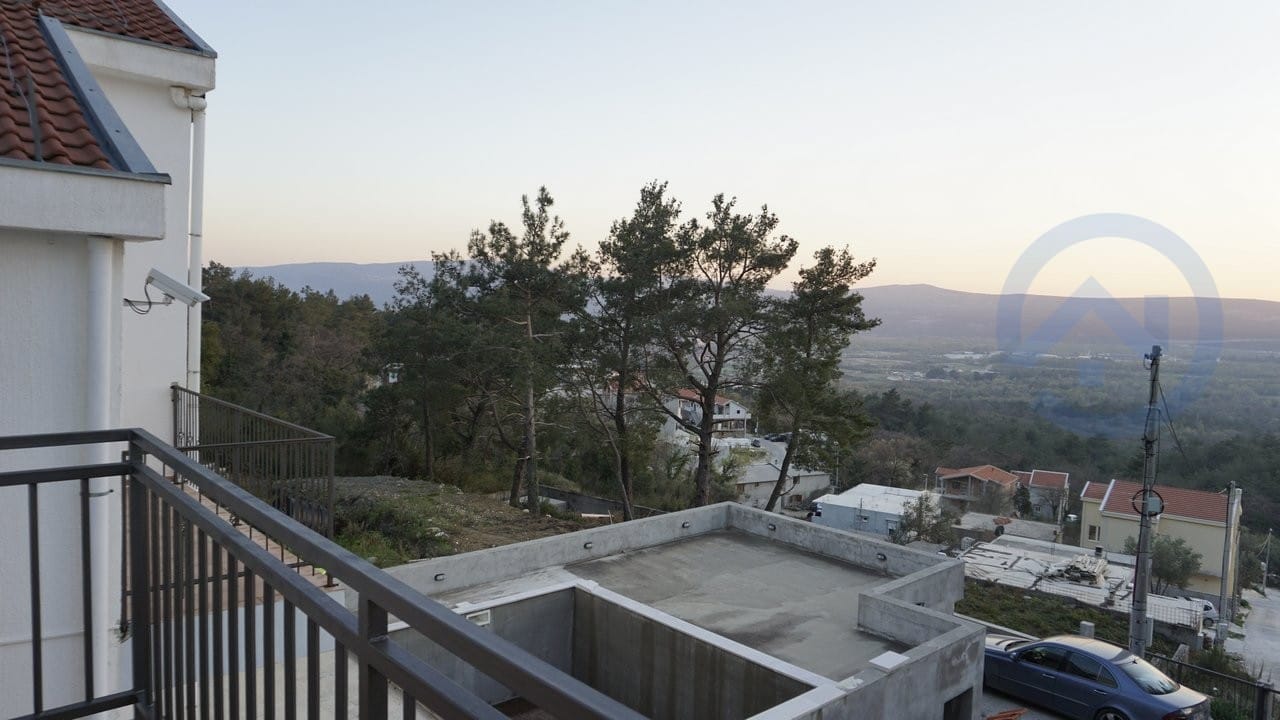 View from the balcony of a house in Kavac, Montenegro: a panorama of mountains, pine forest, and neighboring villas with tiled roofs.