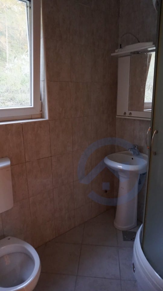 Bathroom in a house, Kavac, Montenegro: beige tiles, shower cabin, sink, and a window with a view of nature.