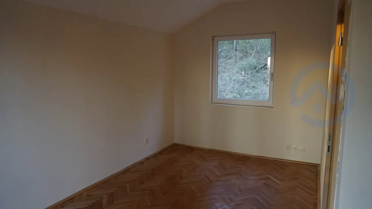Empty room with herringbone parquet flooring and a window overlooking nature.