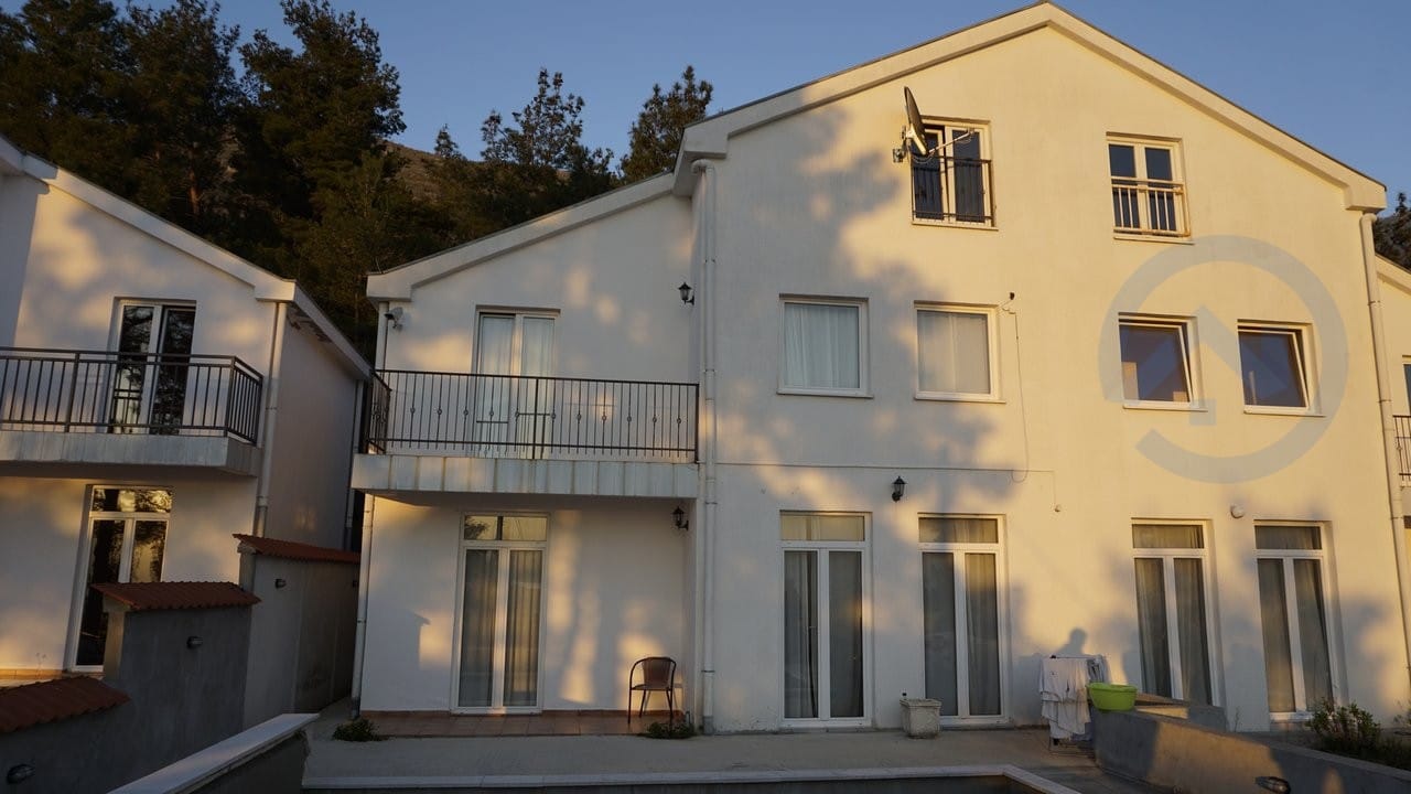 White three-story house with balconies and a terrace in Kavac, Montenegro: view of the building facade in the sunset light.