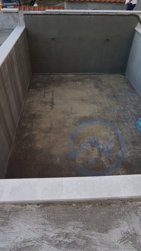 Concrete swimming pool under construction on a house plot in Kavac, Montenegro: view of the basin with light stone finish.