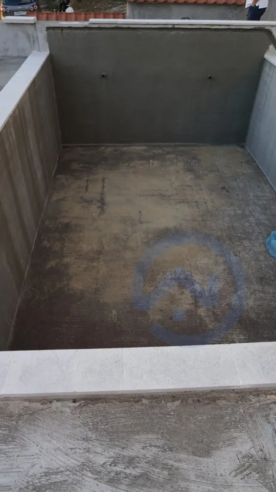 Empty concrete pool base with smooth walls and a logo on the floor, currently under construction or renovation.