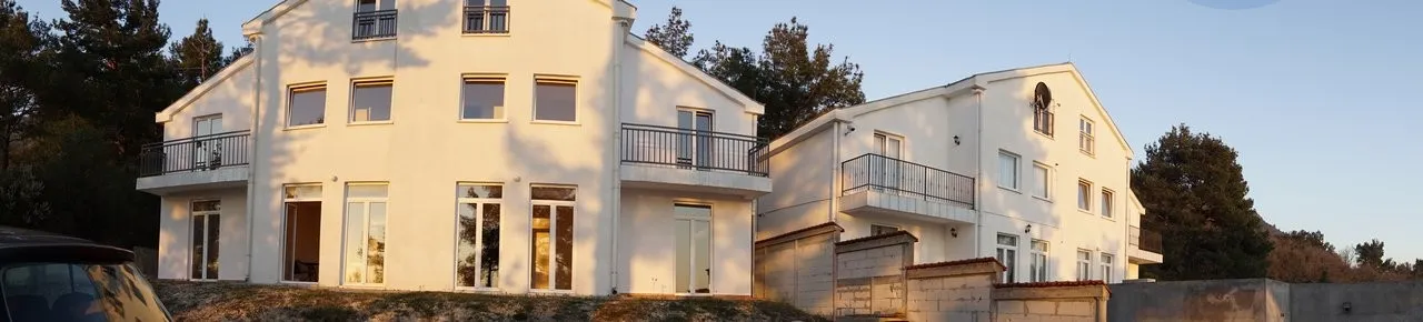 View of a white two-story house with balconies and windows from the outside, surrounded by trees.