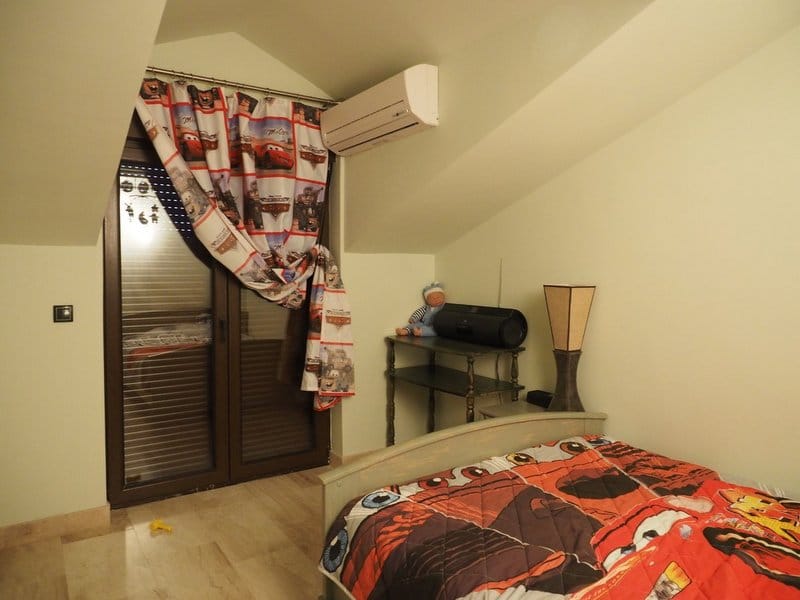 Children’s bedroom in the villa attic in Stoliv, Montenegro: bed, air conditioner, balcony door, and light finishes.