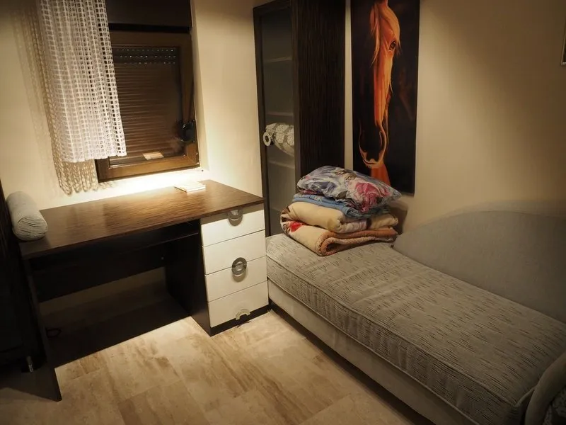 Room with a daybed, desk by the window, and wardrobe. Folded blankets are on the bed, and a horse poster hangs on the wall.