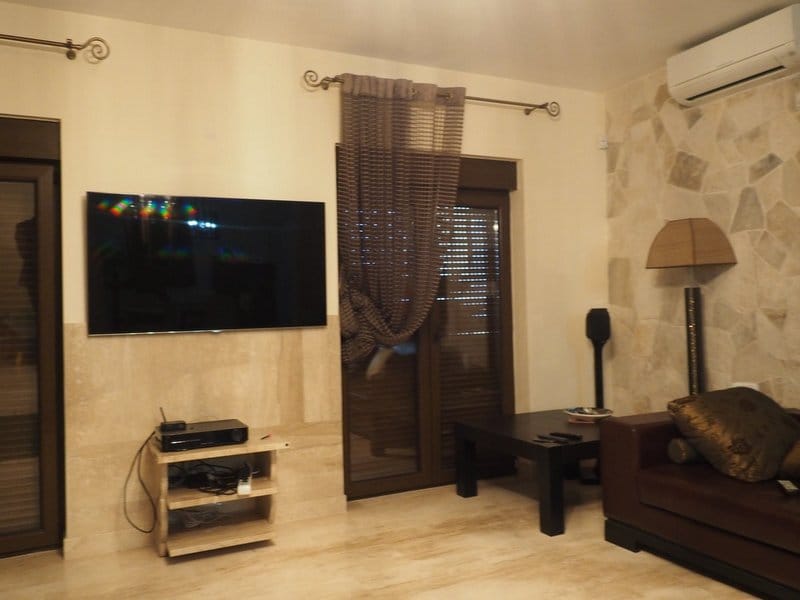 Villa living room in Stoliv, Montenegro: leather sofa, TV area with natural stone finish, and panoramic windows.
