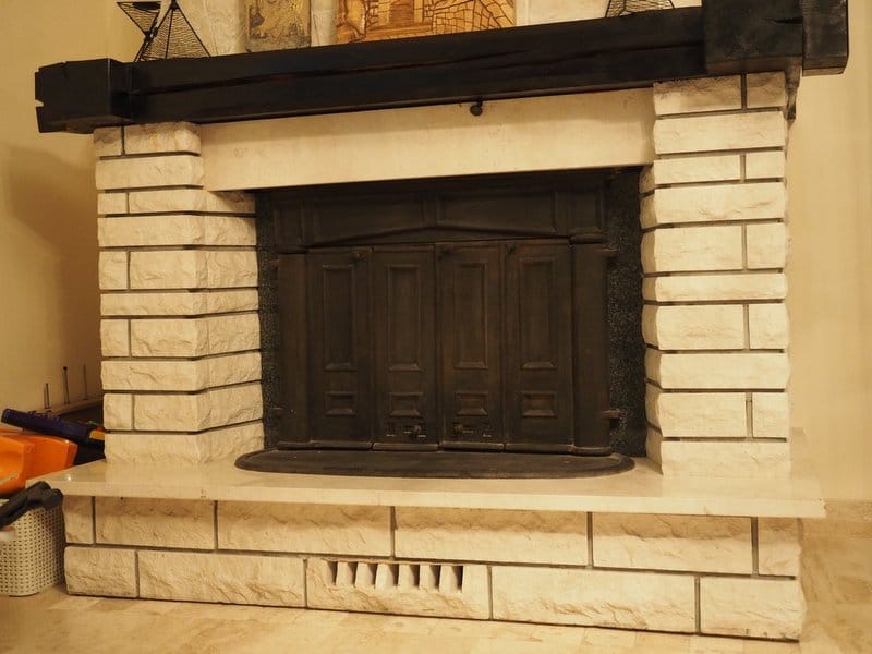 A massive fireplace of light stone with a dark wooden beam in the living room of a villa in Stoliv, Montenegro.
