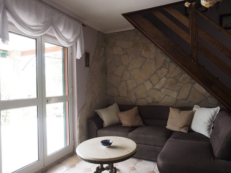 Living room with stone finishes and a staircase in a villa in Dobrota, Montenegro: a cozy sofa and a round table by the window.