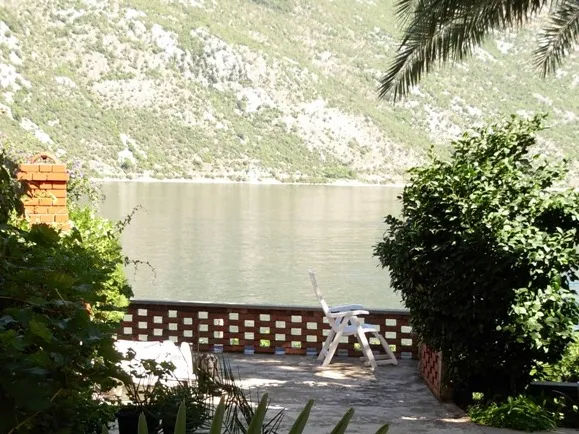 Terrace with a white plastic chair and brick railing overlooking a lake and green mountain slope.