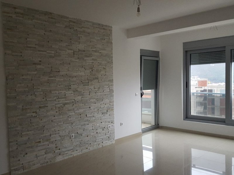 Bright living room in an apartment in Dobrota, Montenegro: an accent wall of decorative stone and access to the balcony.