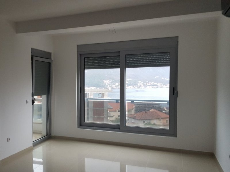 Bright living room in an apartment in Dobrota, Montenegro, with panoramic sea and mountain views through large windows.