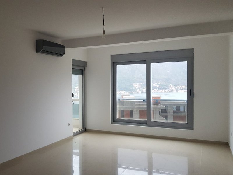 Bright living room in an apartment in Dobrota, Montenegro: panoramic windows with sea view, air conditioning, and tiled floor.