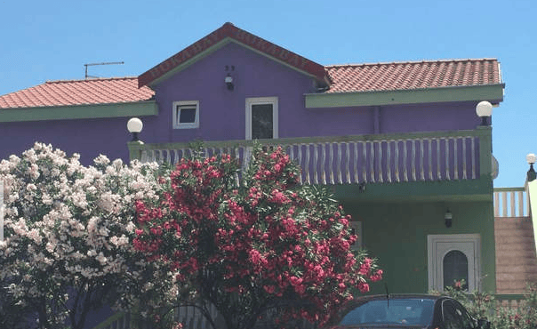 Facade of a two-story house in Igalo, Montenegro, with blooming oleanders, a balcony, and a tiled roof.