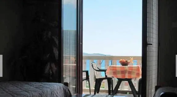 View from a room to a balcony with a table covered in checkered cloth and chairs overlooking the sea.