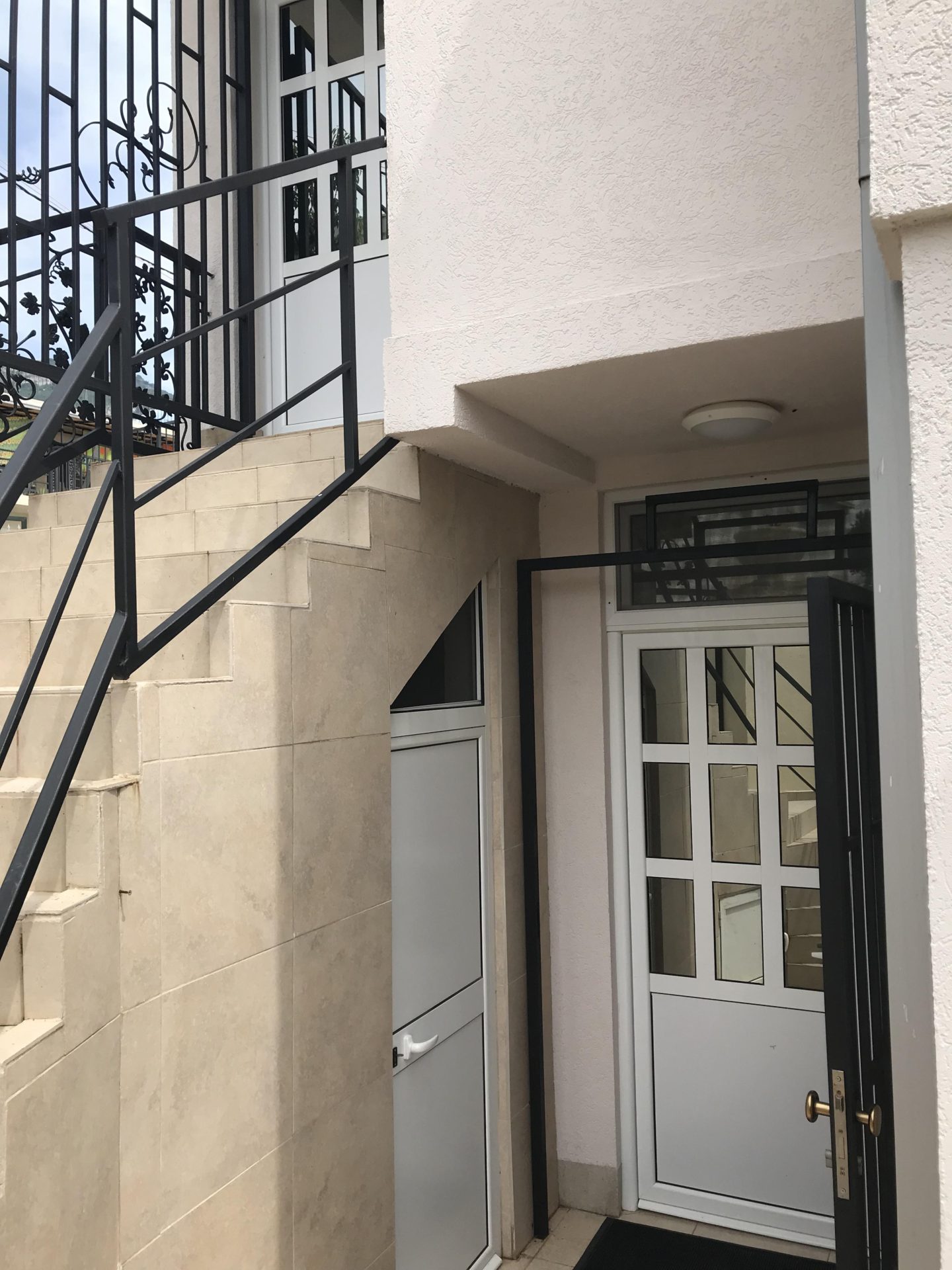Entrance to a house in Bar, Montenegro: white staircase with wrought-iron railings and modern glass-paneled plastic doors.