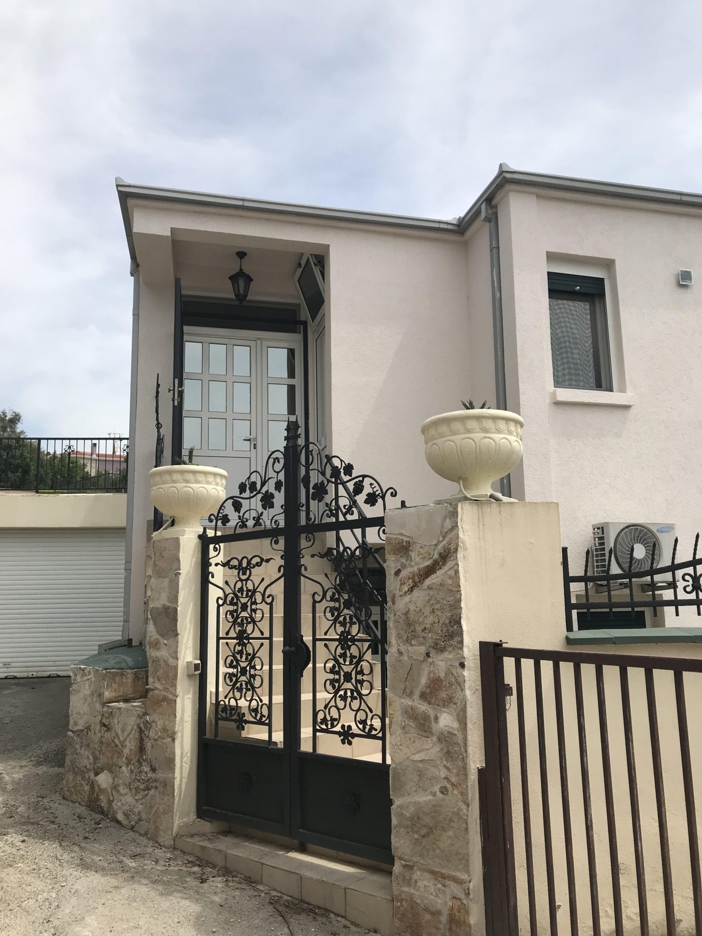 House facade in Bar, Montenegro: entrance area with wrought-iron gates, stone cladding, and decorative planters.