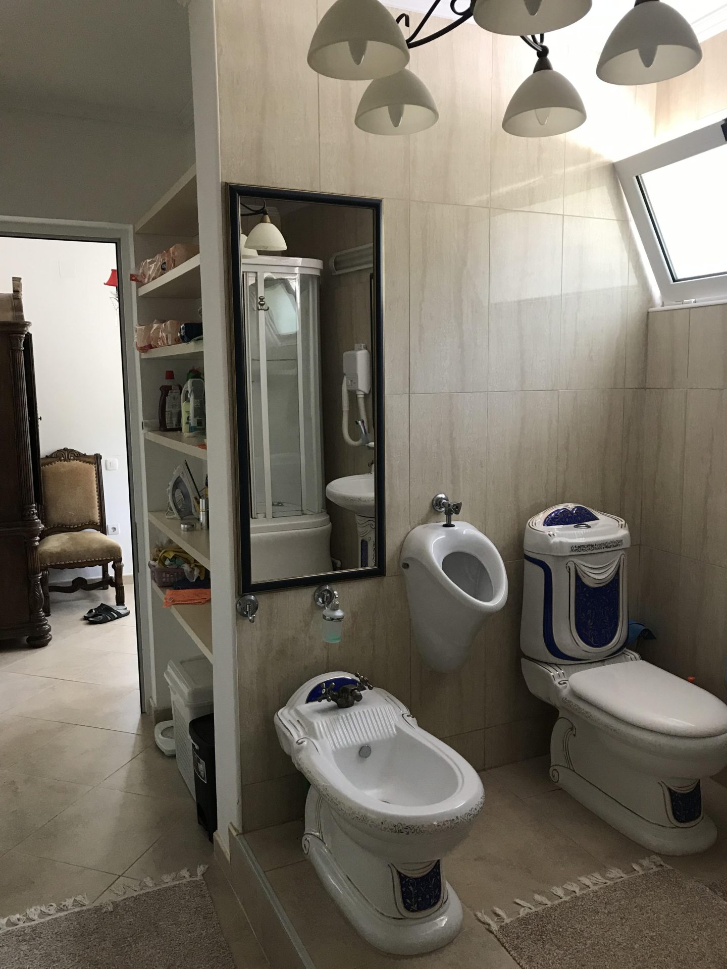 Bathroom with bidet, toilet, and urinal in a house in Bar, Montenegro, finished with light-colored tiles.