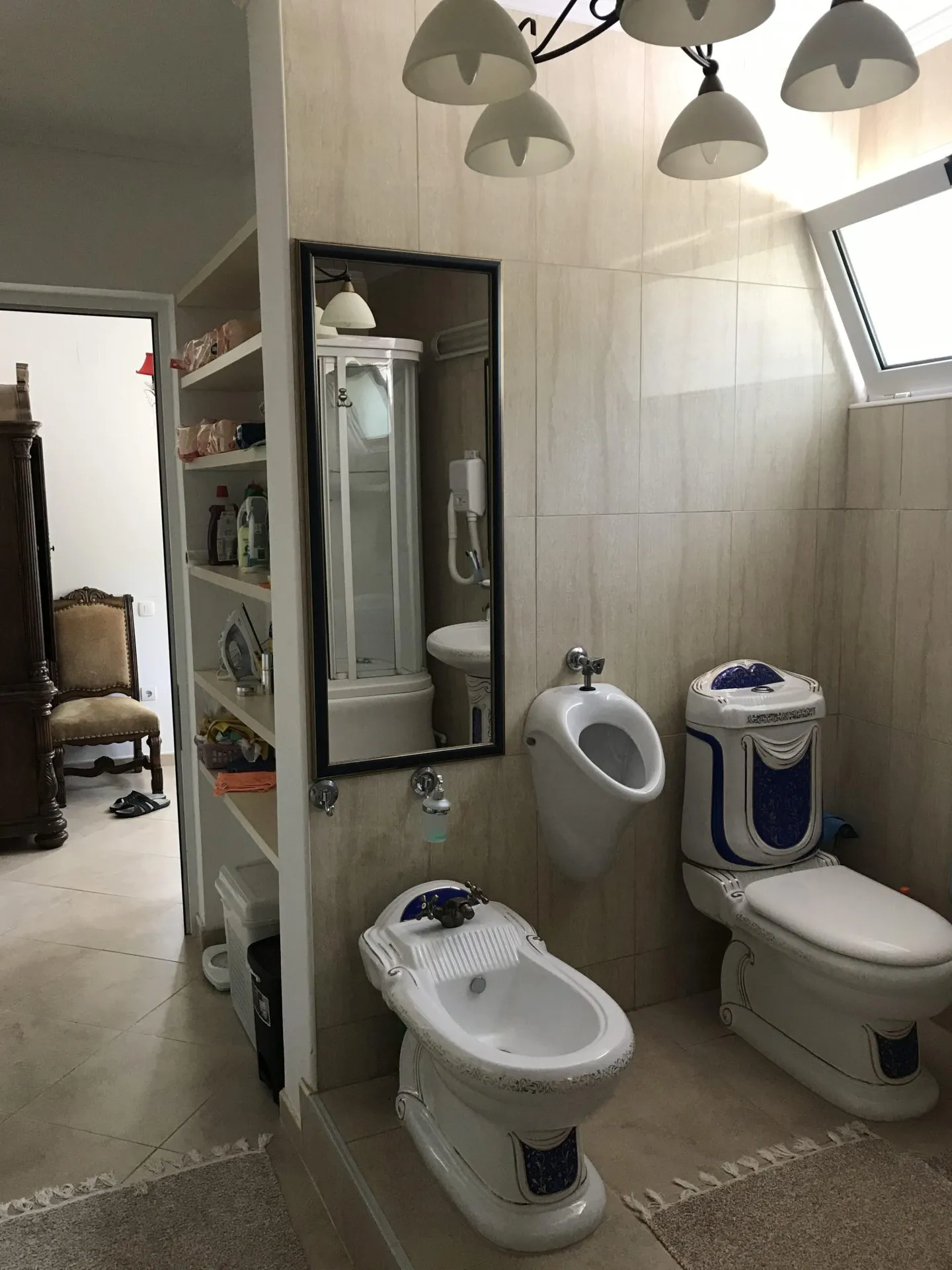 Bathroom featuring a toilet, bidet, and urinal on beige tiled walls.