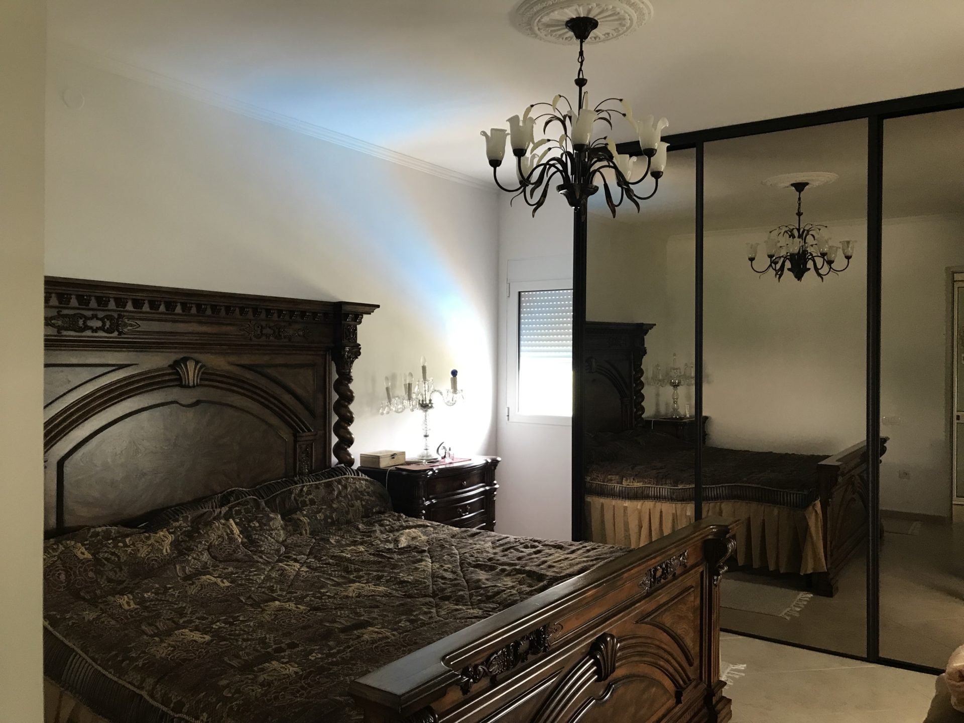 Bedroom in a classic style with a carved wooden bed and mirrored wardrobe in a house, Bar, Montenegro.