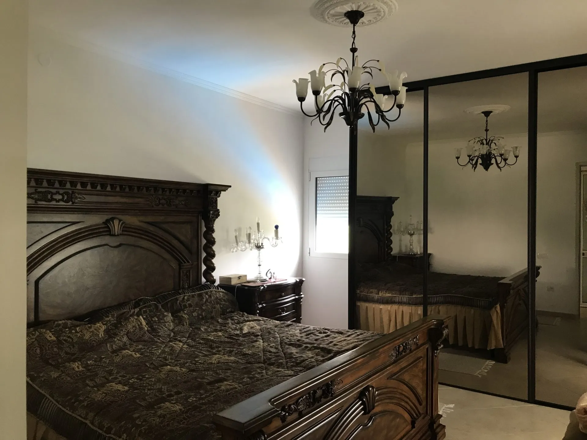 Bedroom featuring a large ornate wooden bed, mirrored wardrobe doors, and a decorative chandelier.