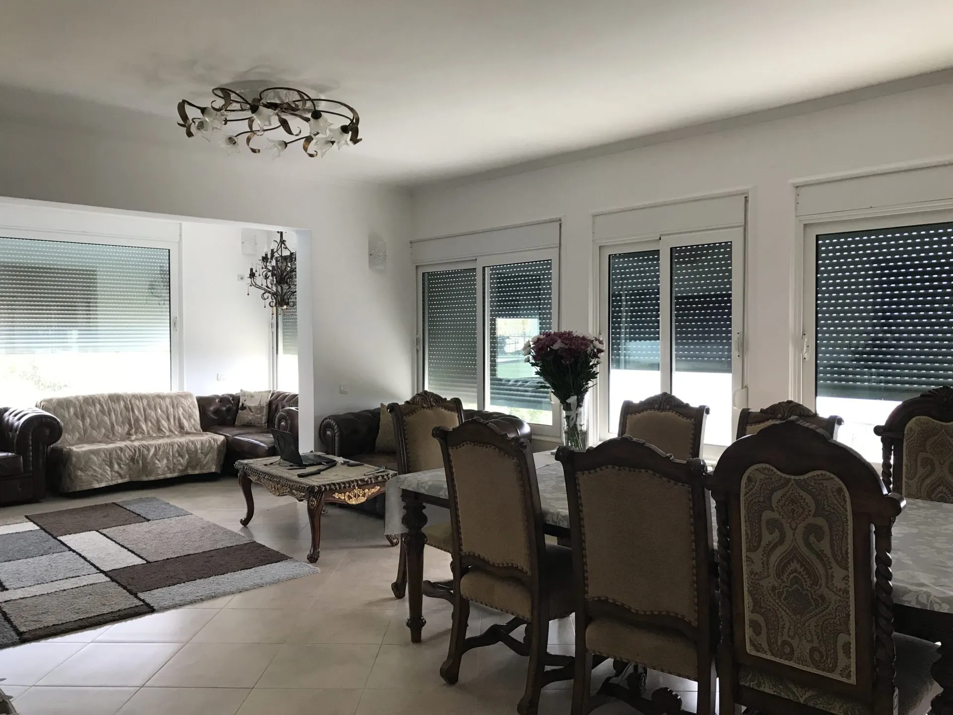 Living room featuring leather sofas, an ornate coffee table, and a wooden dining set near windows.