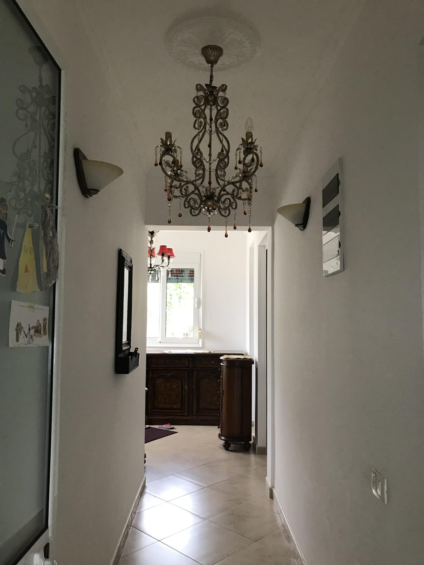Bright hallway with a classic chandelier in a house for sale, Bar, Montenegro: view of antique furniture and a window.