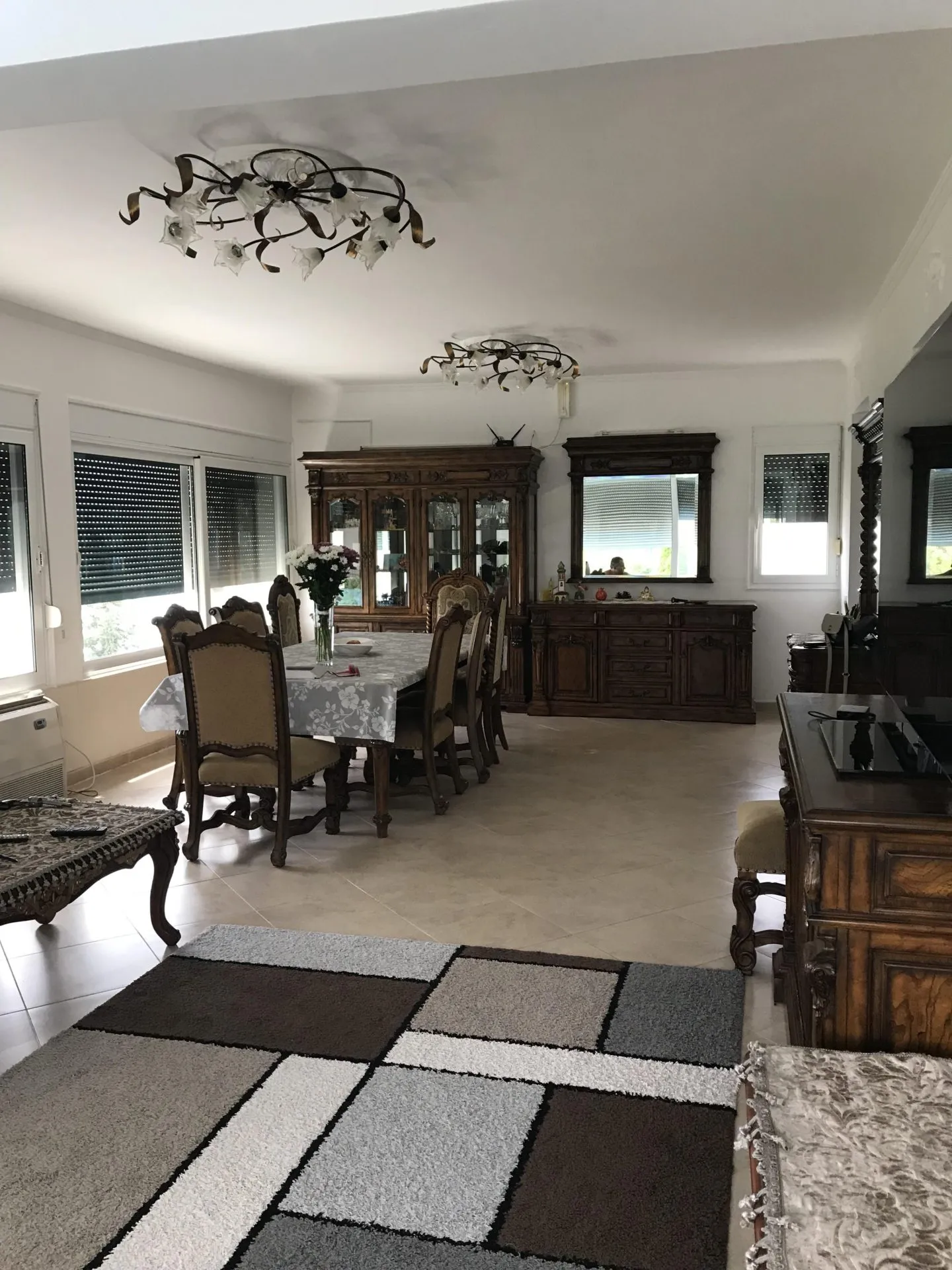 Living room featuring a dining set, ornate wood furniture, geometric rug, and chandeliers.