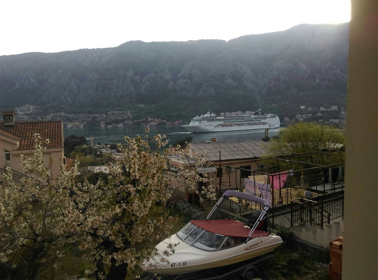 View from the apartment balcony in Kotor, Montenegro: a panoramic bay view with a cruise ship, mountains, and a private boat on the property.