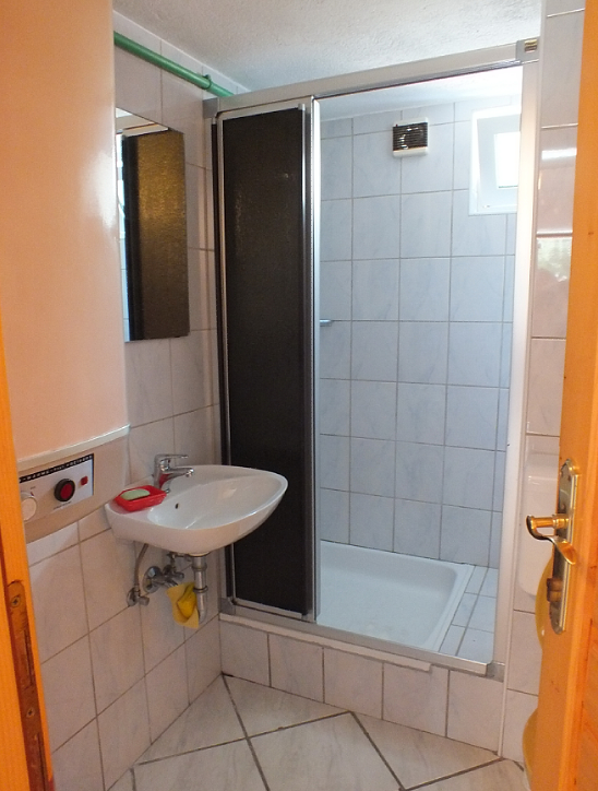Bathroom in a house in Bar, Montenegro: shower cabin, sink, light-colored tiles, and a water heater.