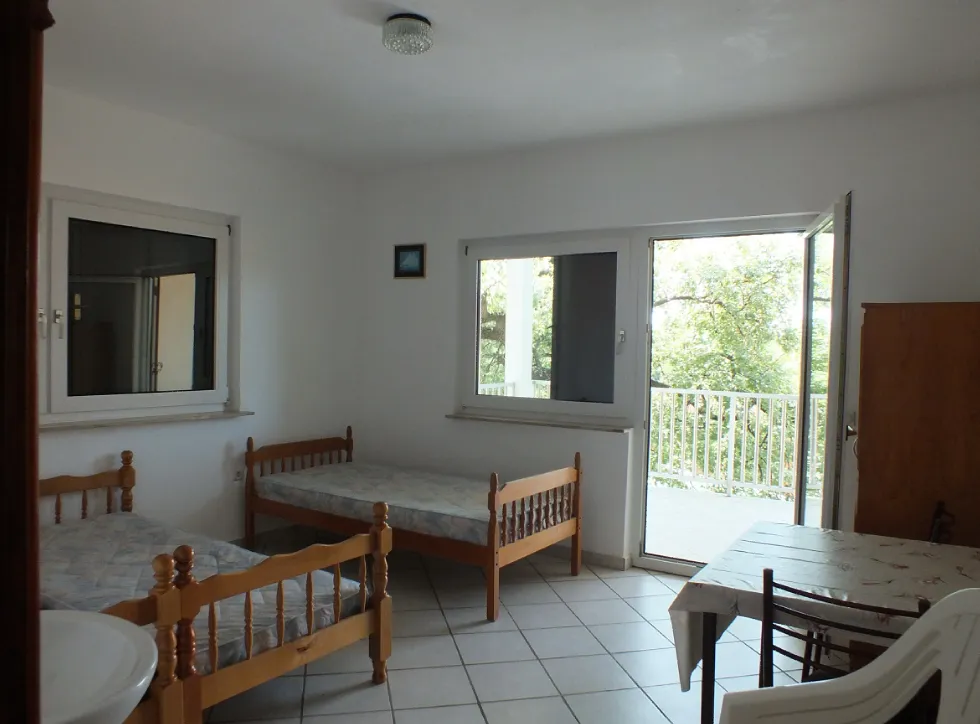 Room with two wooden beds, a dining table, and a glass door leading to a balcony.