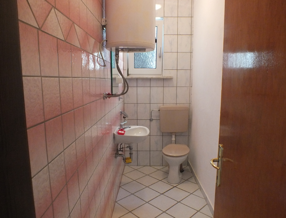 Bathroom with pink tiles, a boiler, and a window in a house for sale, Bar, Montenegro.