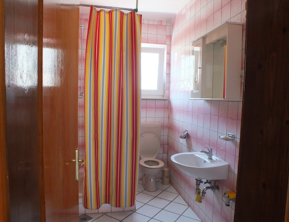 Bathroom in a house in Bar, Montenegro: light tile, a shower area with a bright curtain, a sink, and a toilet.