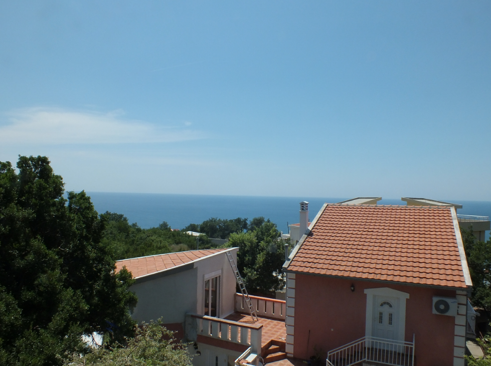 Sea view and the house terrace with a tiled roof in Bar, Montenegro, surrounded by greenery and trees.