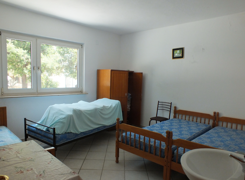 Bright bedroom with three beds and a sink in a house for sale in Bar, Montenegro. View of a green garden.