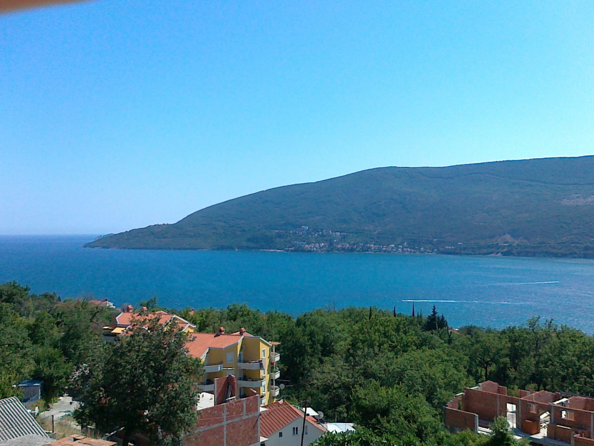 Panoramic sea and mountain view from a house in Herceg Novi, Montenegro: green hills, coastline, and residential buildings.