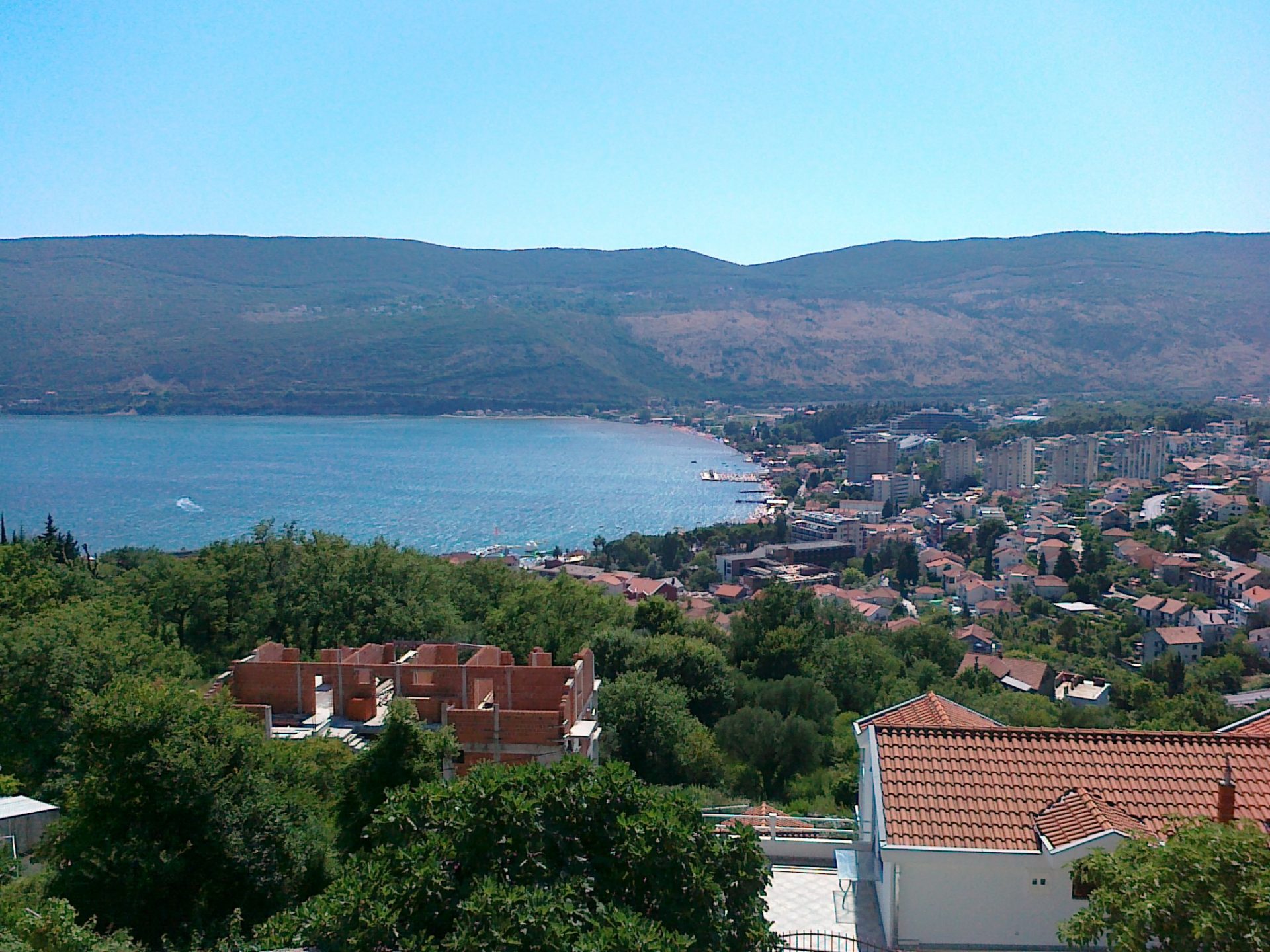 Panoramic view of the sea and the city of Herceg Novi, Montenegro, from the house terrace surrounded by greenery and mountains.