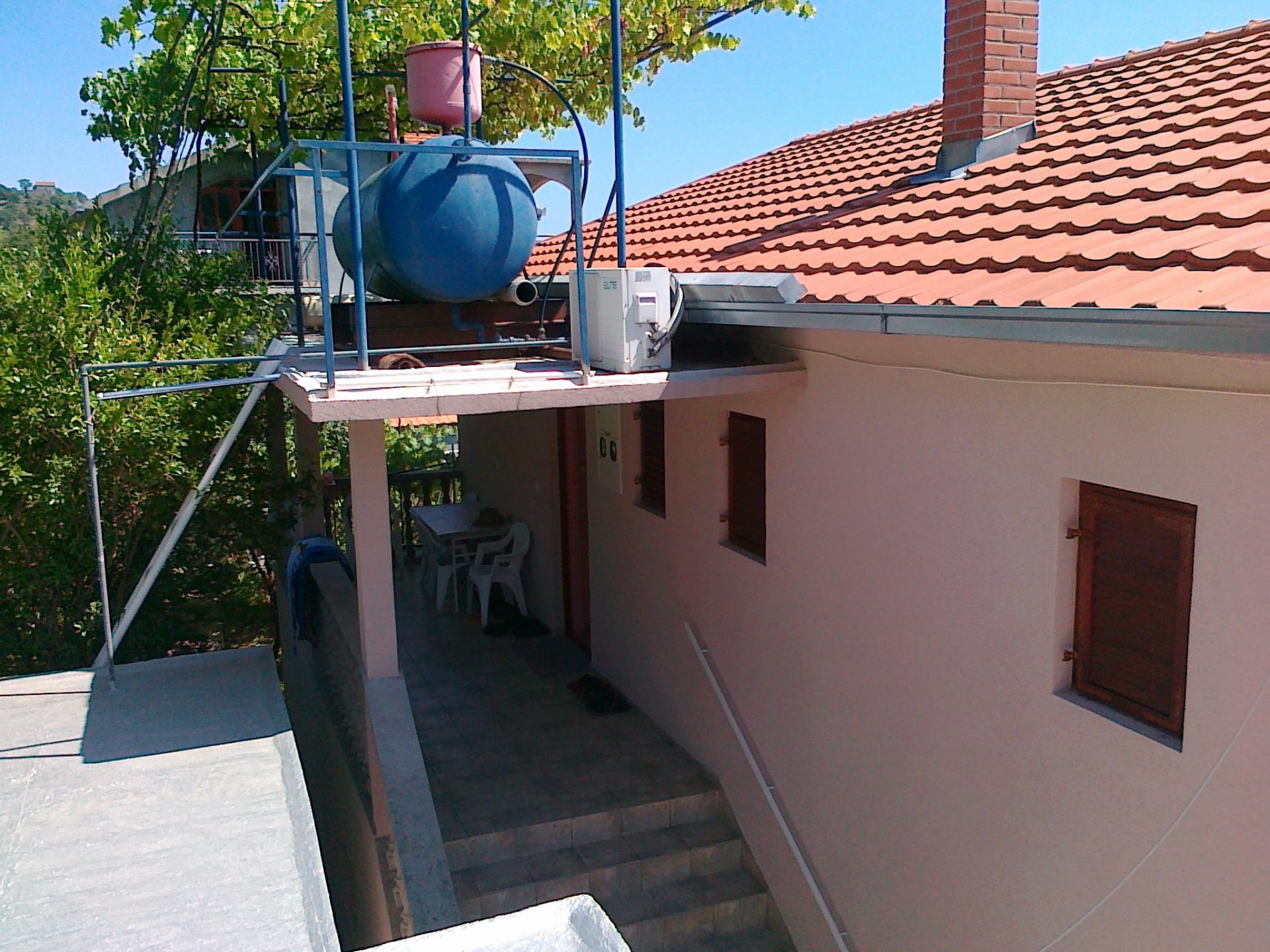 Terrace of a house with a tiled roof and a water tank in Herceg Novi, Montenegro: view of a cozy courtyard with furniture.
