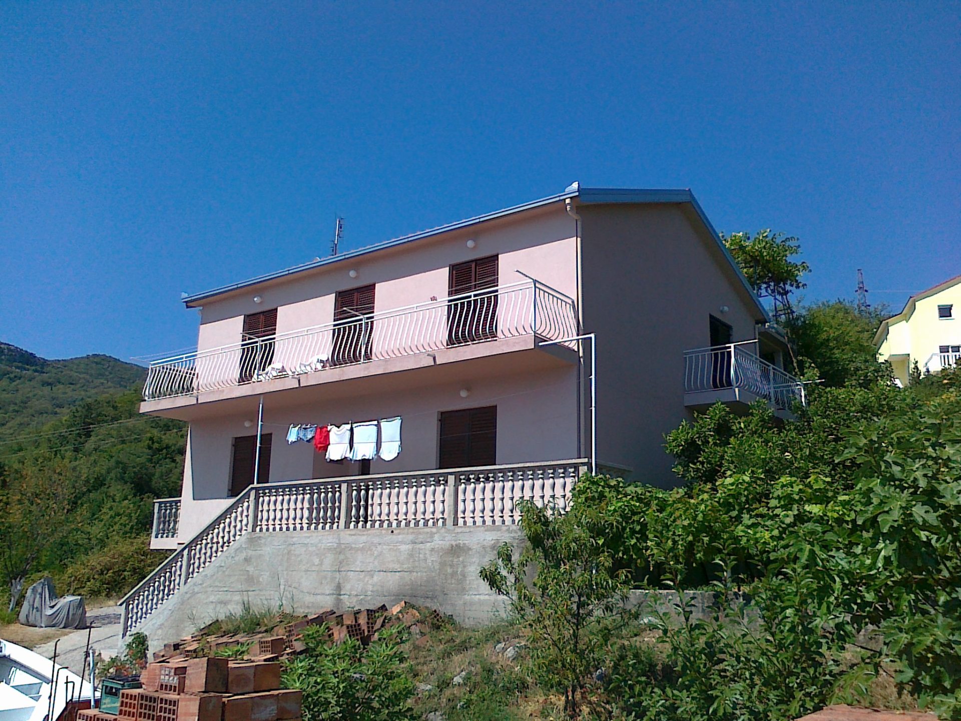 Two-story house with terraces and balustrade in Herceg Novi, Montenegro, front view and green plot.