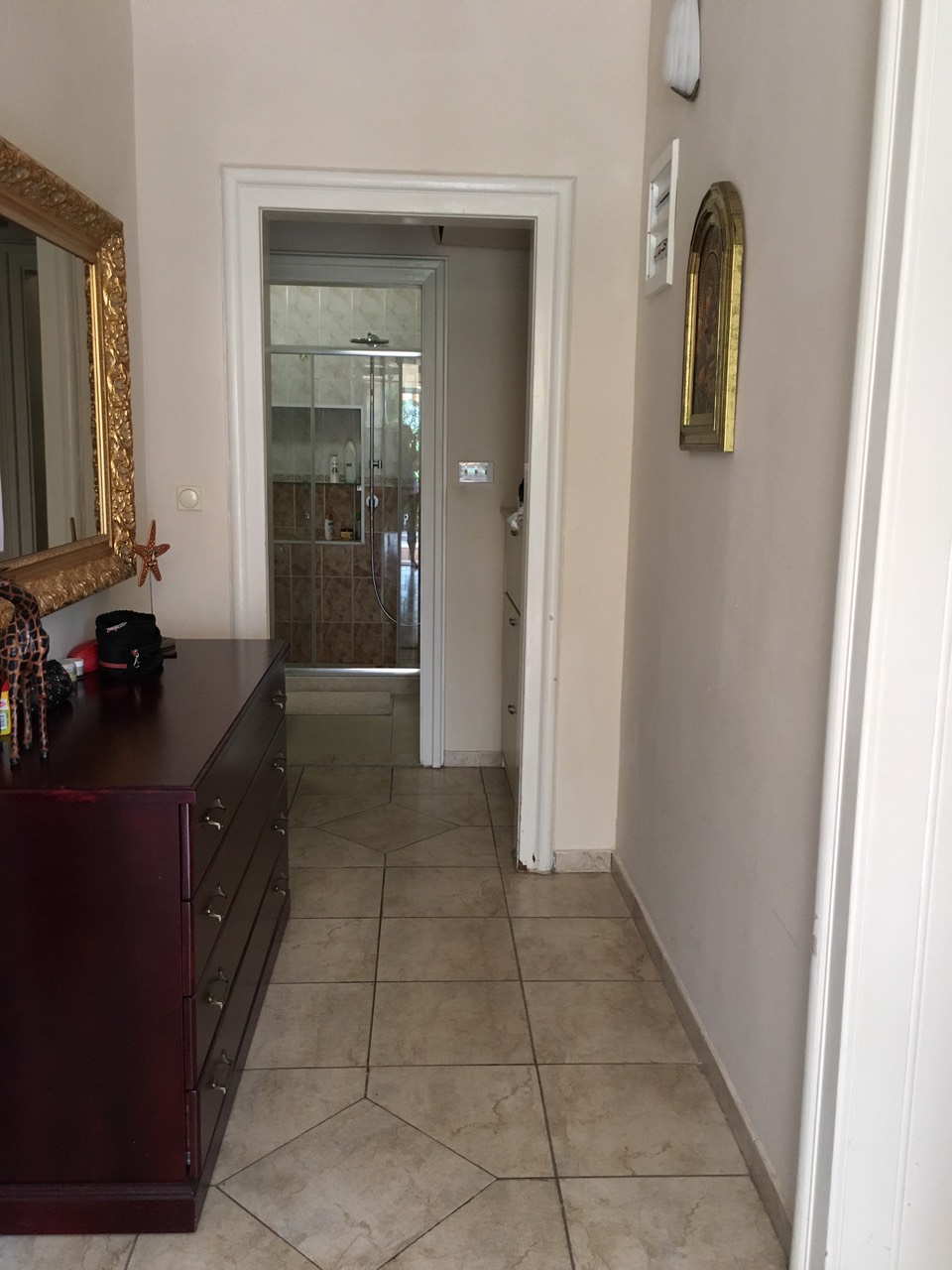 Hallway with a dark dresser and mirror in a house in Herceg Novi, Montenegro, with a view of the bathroom with a shower cabin.