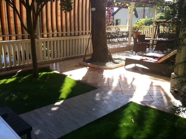 Garden with artificial grass, wooden decking, and patio furniture under a pergola structure.