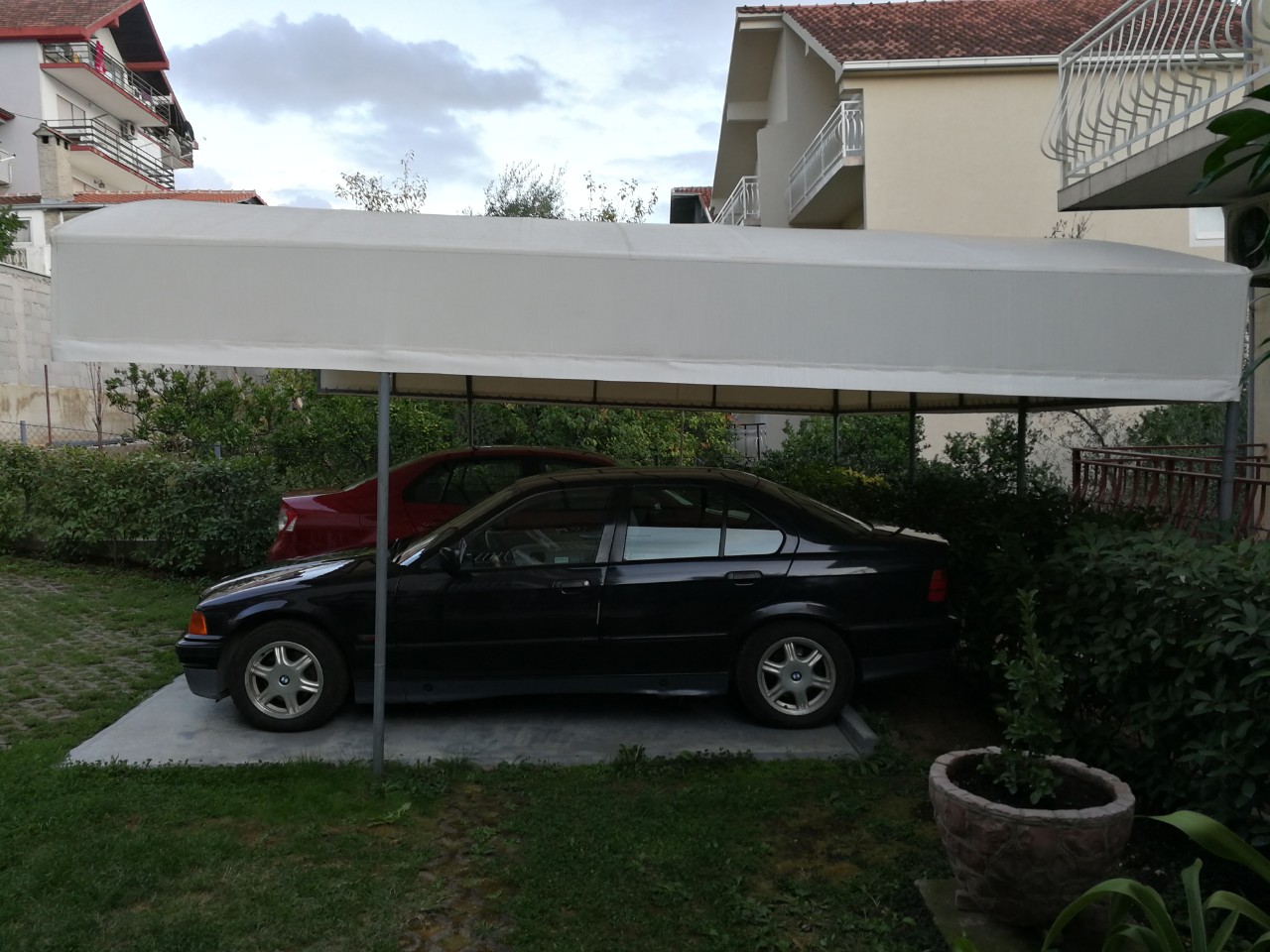Covered parking for cars on a private property in Tivat, Montenegro, with a green garden and canopy.